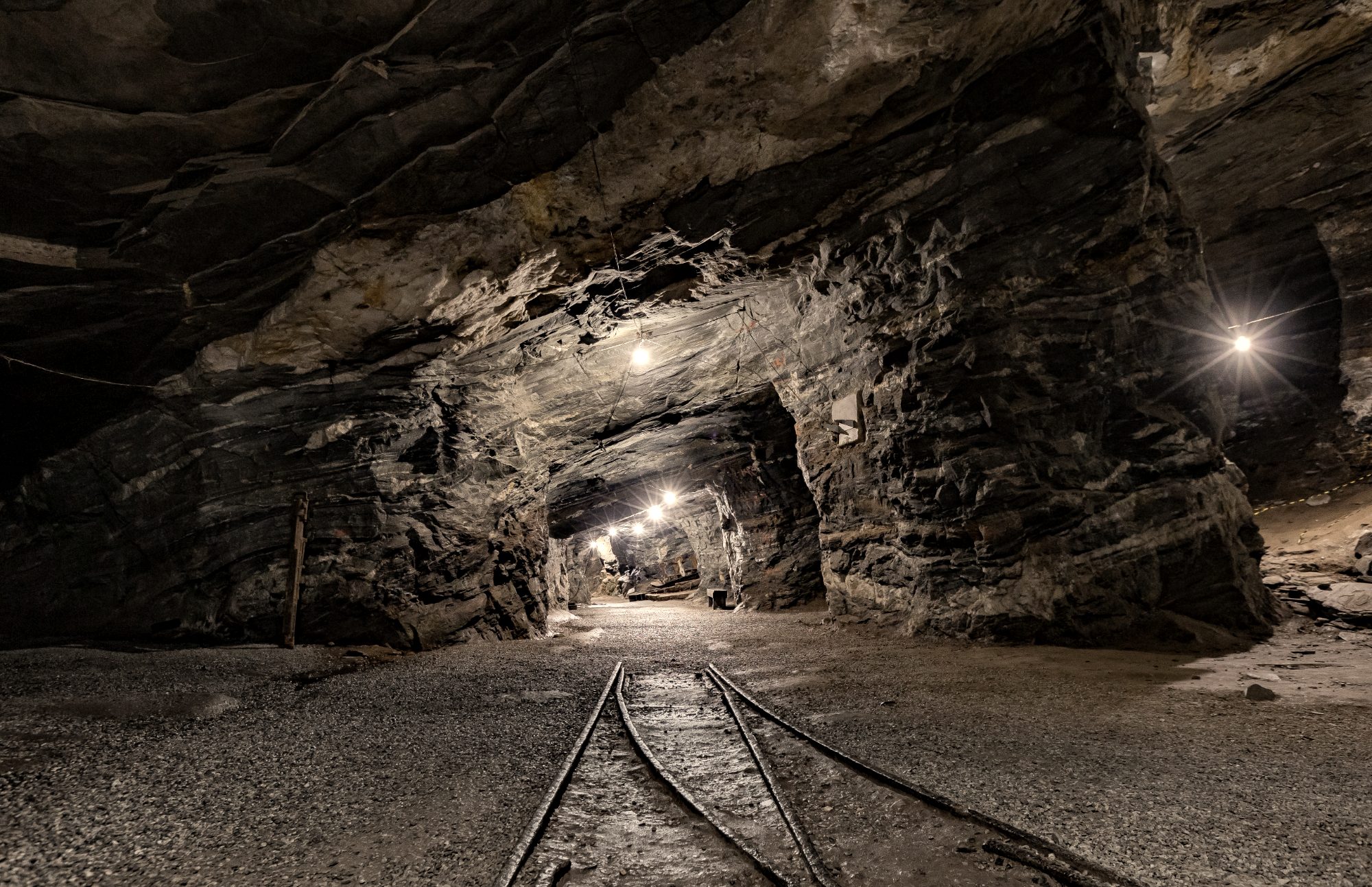 Lit underground mine tunnel with rail tracks running into the rock