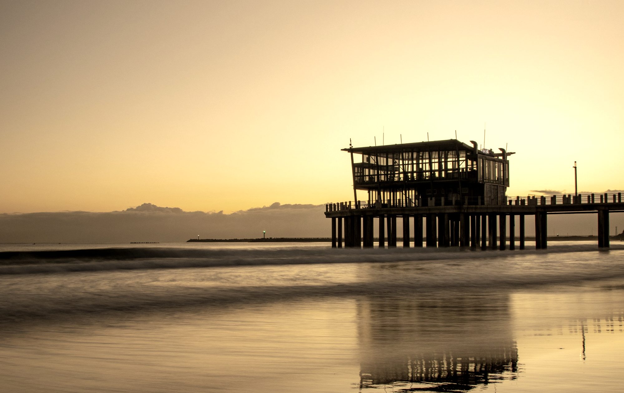 Pier on stilts silhouetted against a golden sunrise over the sea at Durban's Point